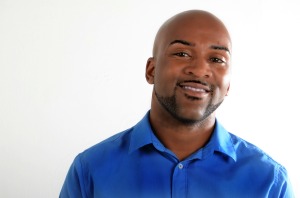 Headshot of Drew Anderson, a handsome Black man with a trimmed beard clean shaved head. He is wearing a royal blue button-up shirt and looking directly into the camera.